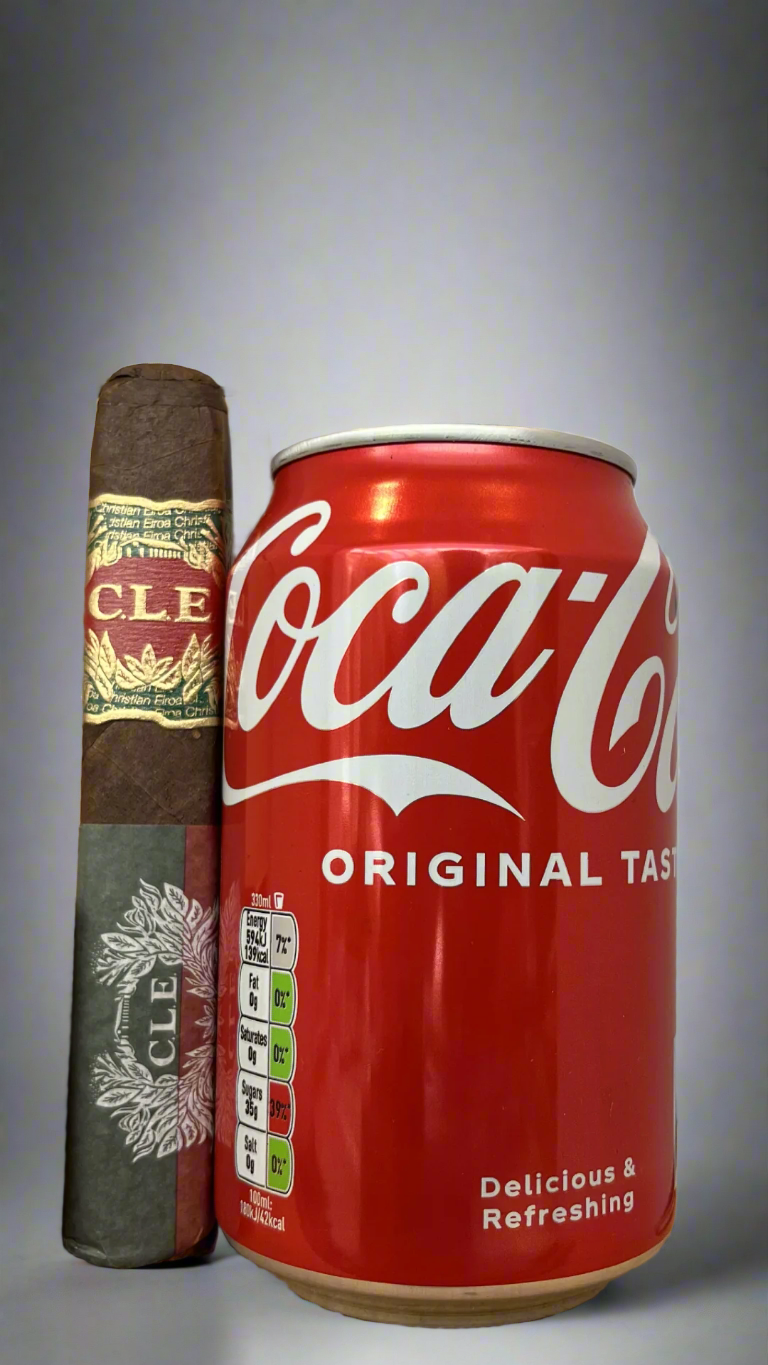 A single C.L.E 25th Anniversary Robusto cigar next to a can of coca cola, the cigar is a few centimetres taller than the can.