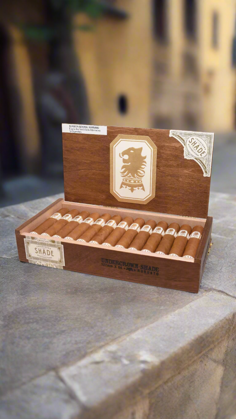 a box of Drew Estate Undercrown Shade Robusto cigars against a castle courtyard backdrop.