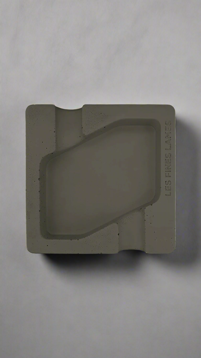 A square shaped deep olive green moulded concrete ashtray with a cigar holder on opposite ends. There is a large rhombus shaped cavity in the middle of the ashtray to collect ash.