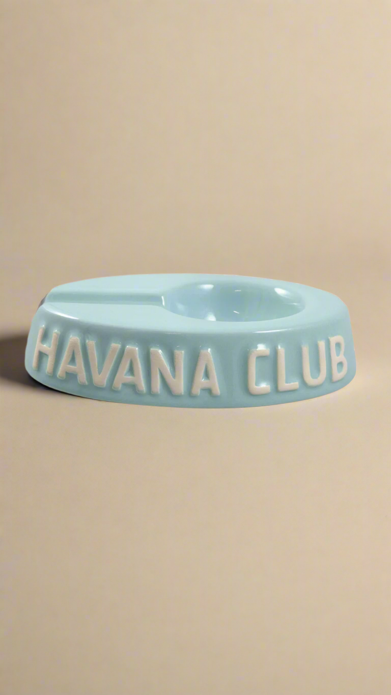 A oval shaped light blue glazed ceramic ashtray with a cigar holder on one of the long ends. The words Havana club are embossed on the side, the lettering is unglazed.