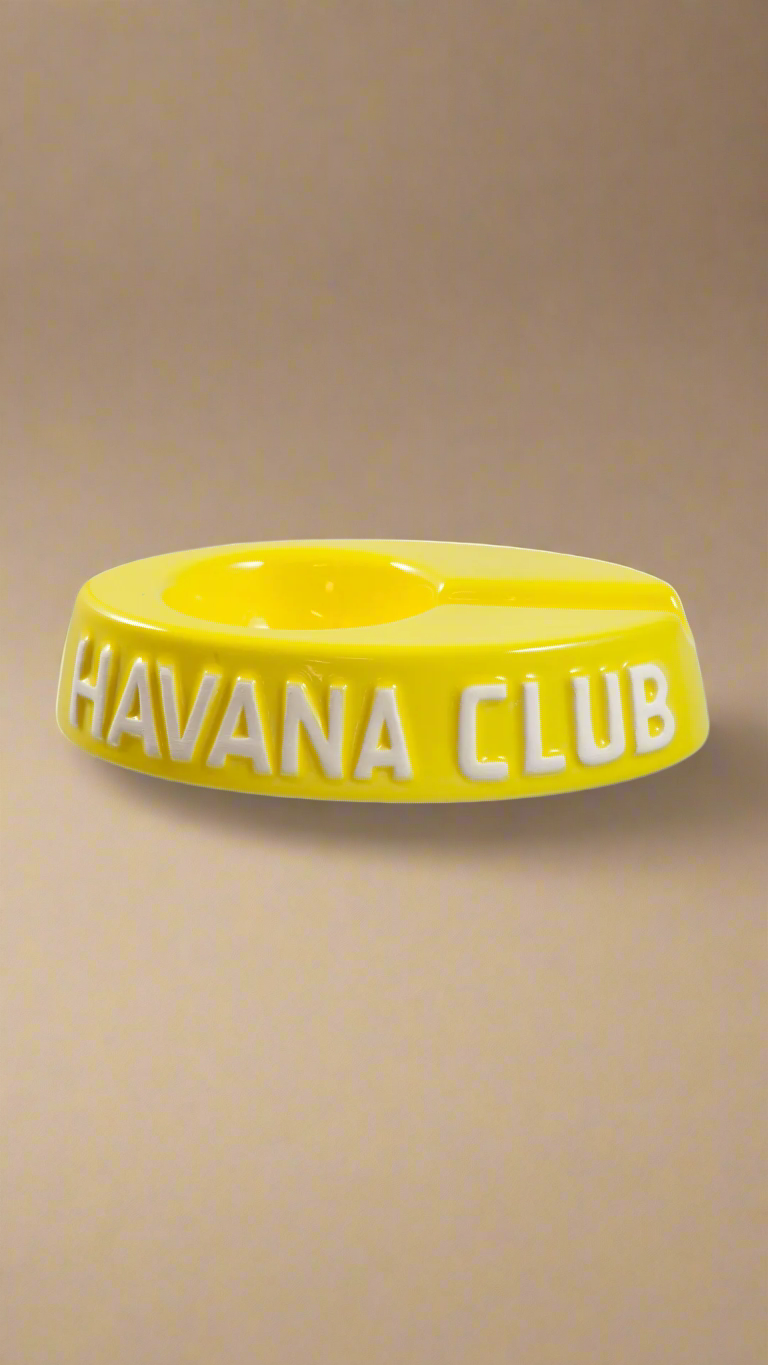 A oval shaped bright yellow glazed ceramic ashtray with a cigar holder on one of the long ends. The words Havana club are embossed on the side, the lettering is unglazed.