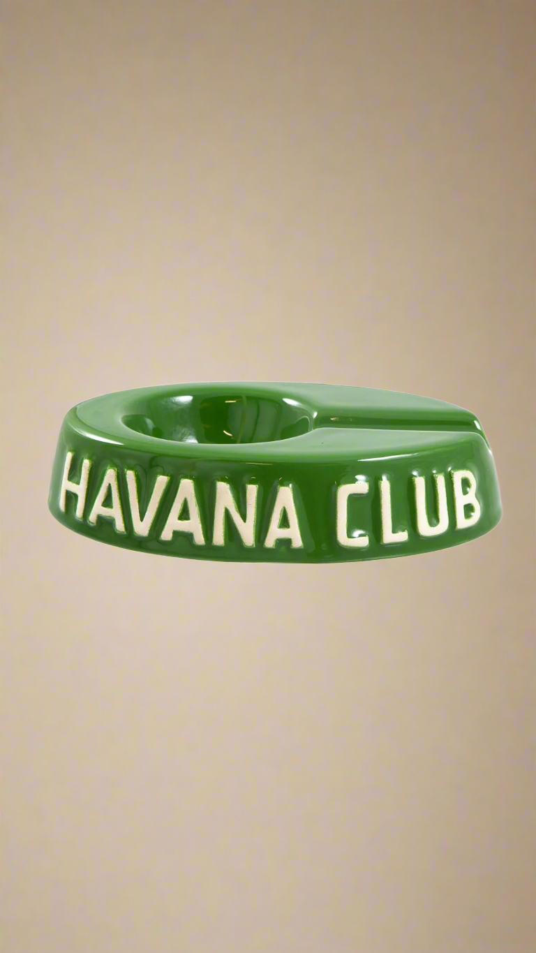 A oval shaped green glazed ceramic ashtray with a cigar holder on one of the long ends. The words Havana club are embossed on the side, the lettering is unglazed.