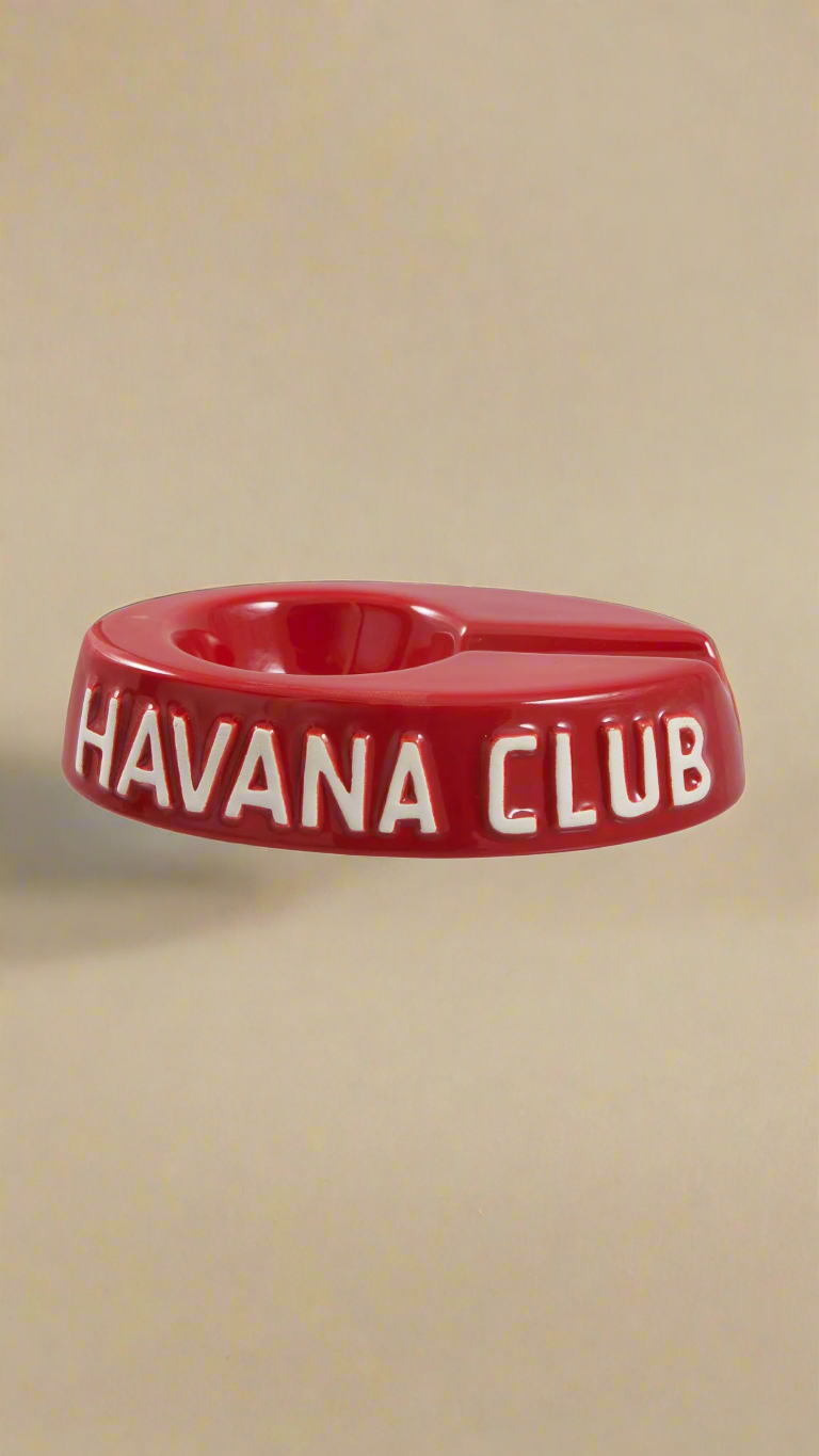 A oval shaped bright red glazed ceramic ashtray with a cigar holder on one of the long ends. The words Havana club are embossed on the side, the lettering is unglazed.