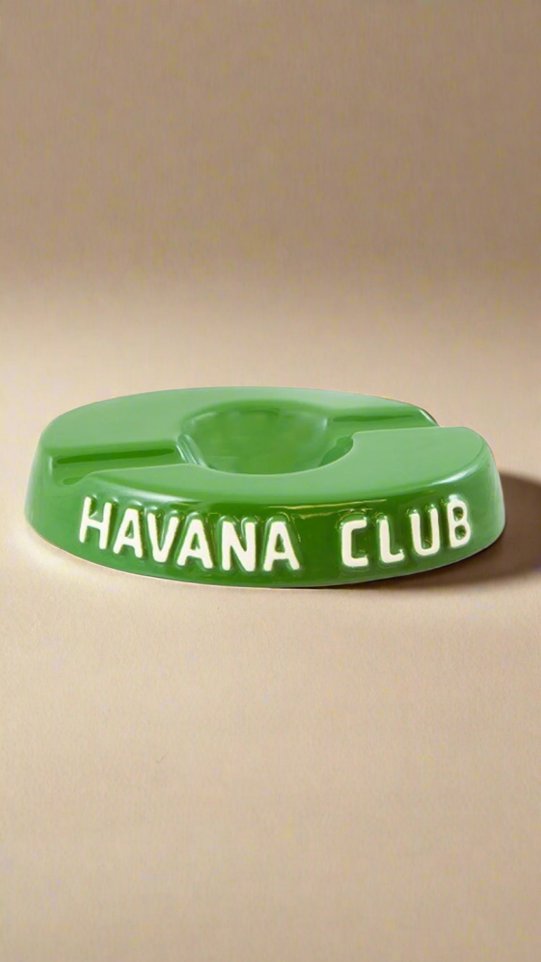 A oval shaped bottle green glazed ceramic ashtray with two cigar holders on opposite sides. The words Havana club are embossed on the side, the words are in raw ceramic.