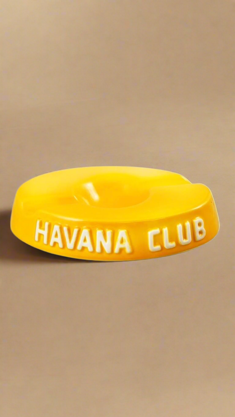 A oval shaped bright yellow glazed ceramic ashtray with two cigar holders on opposite sides. The words Havana club are embossed on the side, the lettering is unglazed.