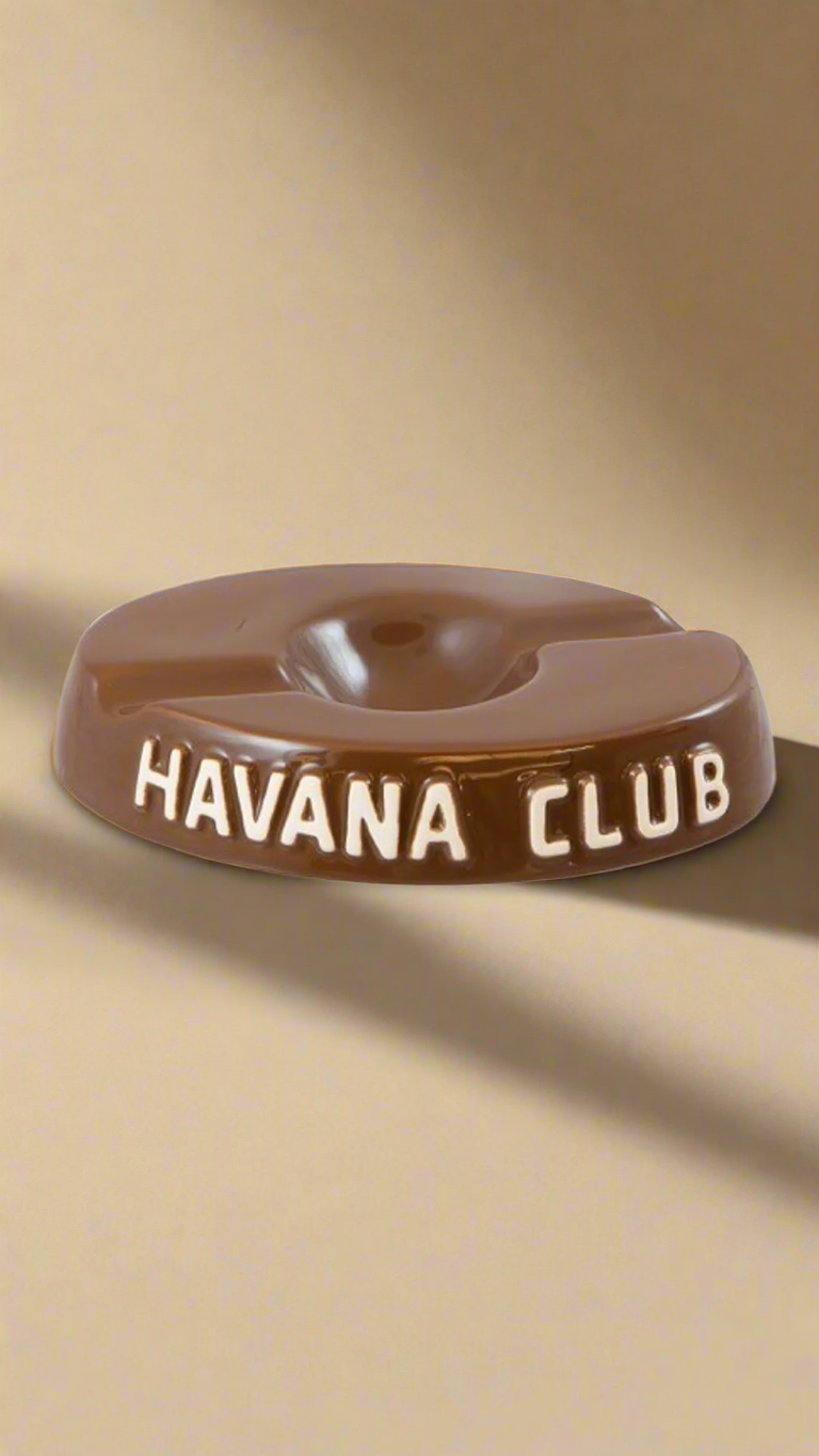 A oval shaped chocolate brown glazed ceramic ashtray with two cigar holders on opposite sides. The words Havana club are embossed on the side, the lettering is unglazed.