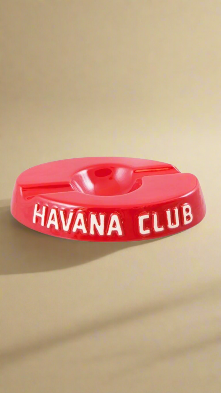 A oval shaped bright red glazed ceramic ashtray with two cigar holders on opposite sides. The words Havana club are embossed on the side, the lettering is unglazed.