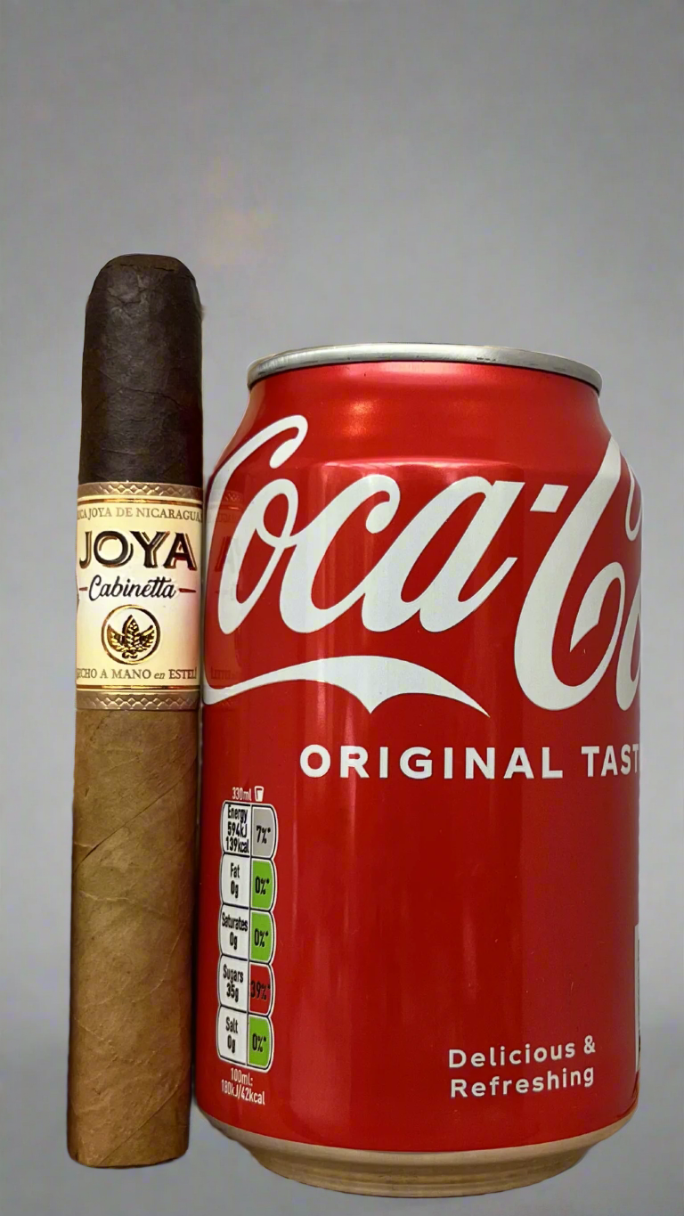 A single Joya De Nicaragua Cabinetta Corona Gorda next to a can of coca cola to show the scale, the cigar is a few centimetres bigger than the can.