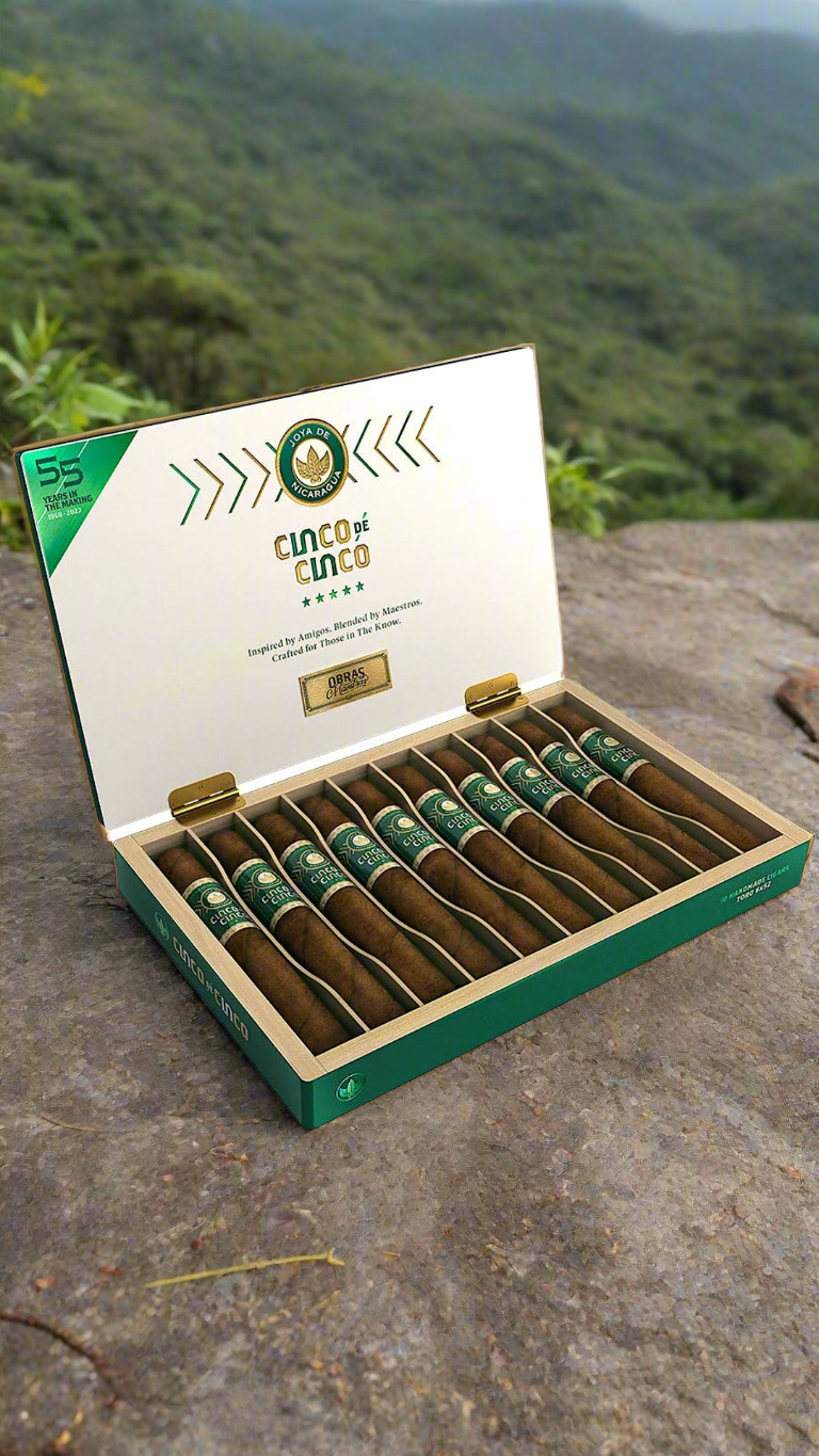 A box of Joya De Nicaragua Cinco De Cinco Robusto cigars, in a mountainous region.