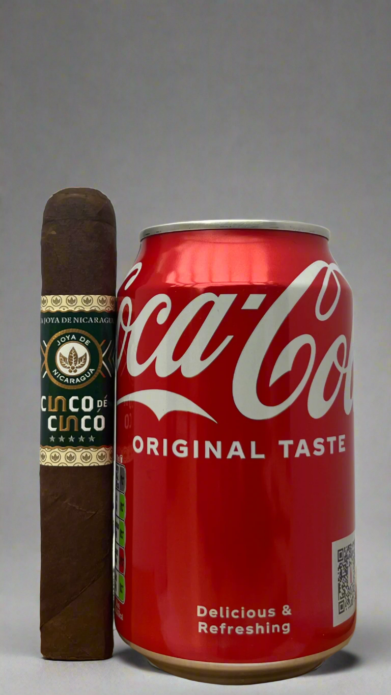 A single Joya De Nicaragua Cinco De Cinco Robusto next to a can of coca cola to show scale. The cigar is slightly longer than the can.