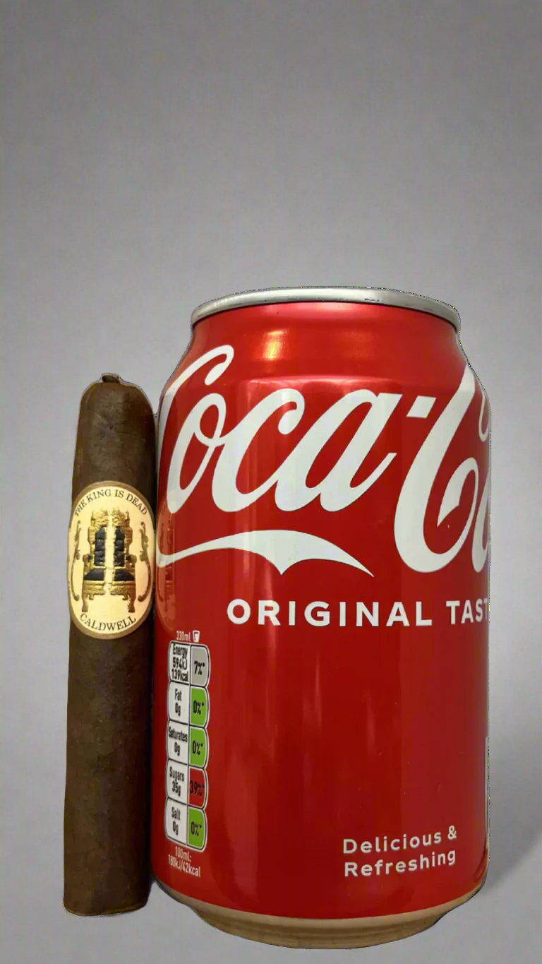 A single Caldwell King is Dead Manzanita Cigar next to a can of coca cola to show scale, the cigar is slightly shorter than the can.