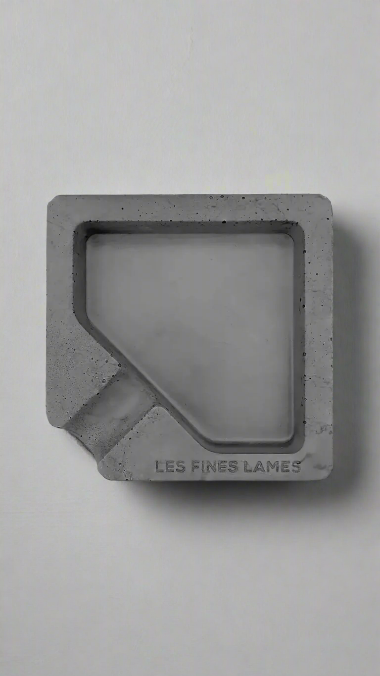 A square shaped dark grey moulded concrete ashtray with a cigar holder on one corner. There is a large diamond shaped cavity in the middle of the ashtray to collect ash.