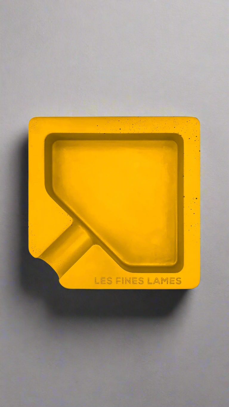 A square shaped yellow moulded concrete ashtray with a cigar holder on one corner. There is a large diamond shaped cavity in the middle of the ashtray to collect ash