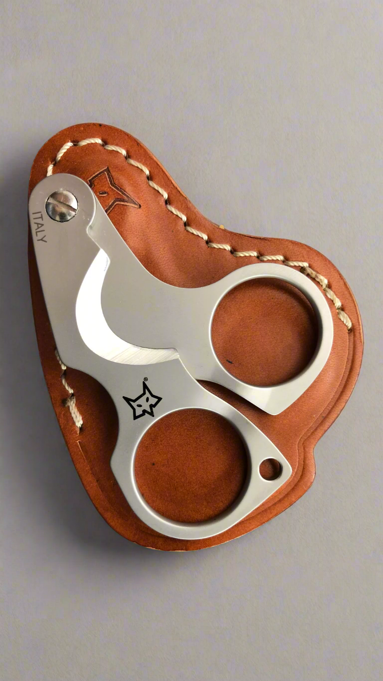 A matte finished stainless steel cigar cutter that looks like a pair of scissors on top of a brown sticked leather case.