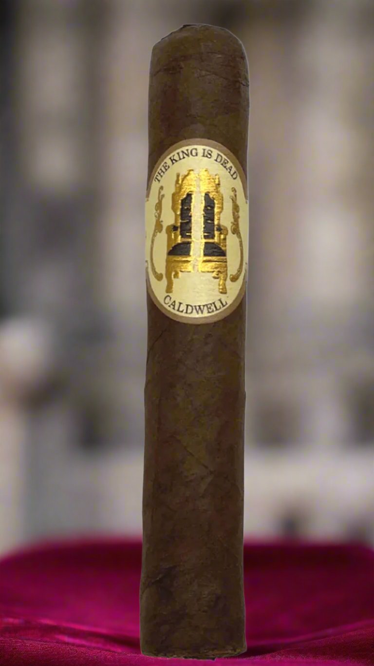 A single Caldwell The King is Dead Manzanita cigar standing on a red velvet pillow.