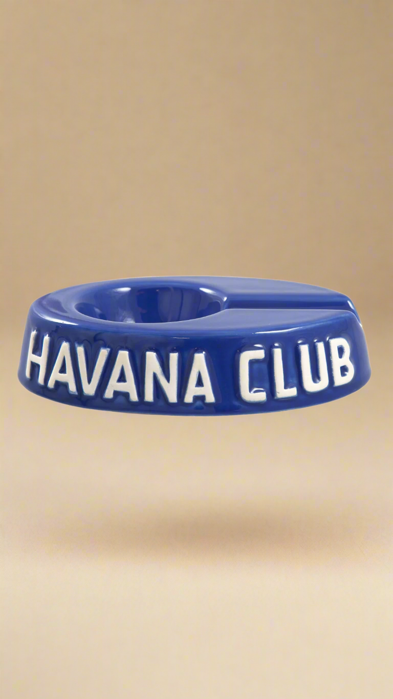 A oval shaped blue glazed ceramic ashtray with a cigar holder on one of the long ends. The words Havana club are embossed on the side, the lettering is unglazed.