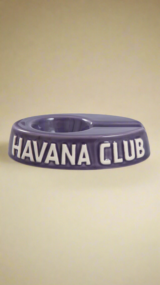 A oval shaped purple glazed ceramic ashtray with a cigar holder on one of the long ends. The words Havana club are embossed on the side, the lettering is unglazed.