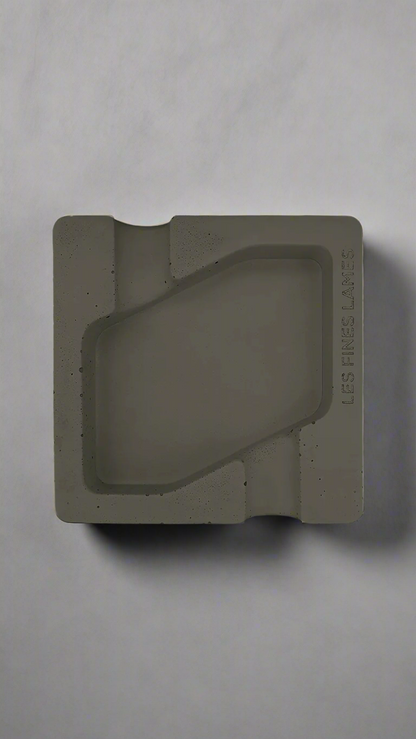A square shaped deep olive green moulded concrete ashtray with a cigar holder on opposite ends. There is a large rhombus shaped cavity in the middle of the ashtray to collect ash.