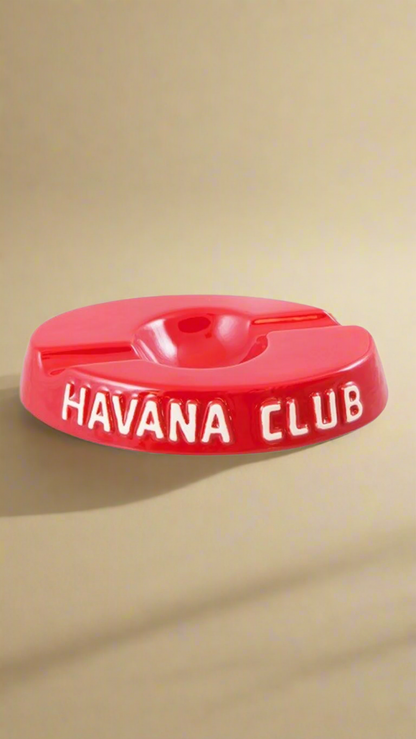 A oval shaped bright red glazed ceramic ashtray with two cigar holders on opposite sides. The words Havana club are embossed on the side, the lettering is unglazed.