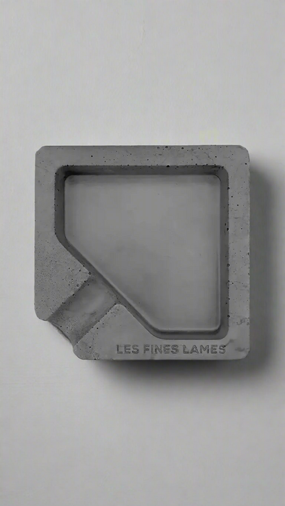 A square shaped dark grey moulded concrete ashtray with a cigar holder on one corner. There is a large diamond shaped cavity in the middle of the ashtray to collect ash.