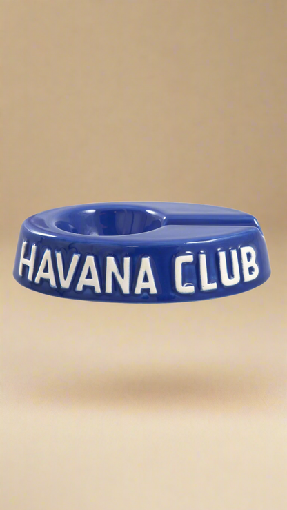 A oval shaped blue glazed ceramic ashtray with a cigar holder on one of the long ends. The words Havana club are embossed on the side, the lettering is unglazed.